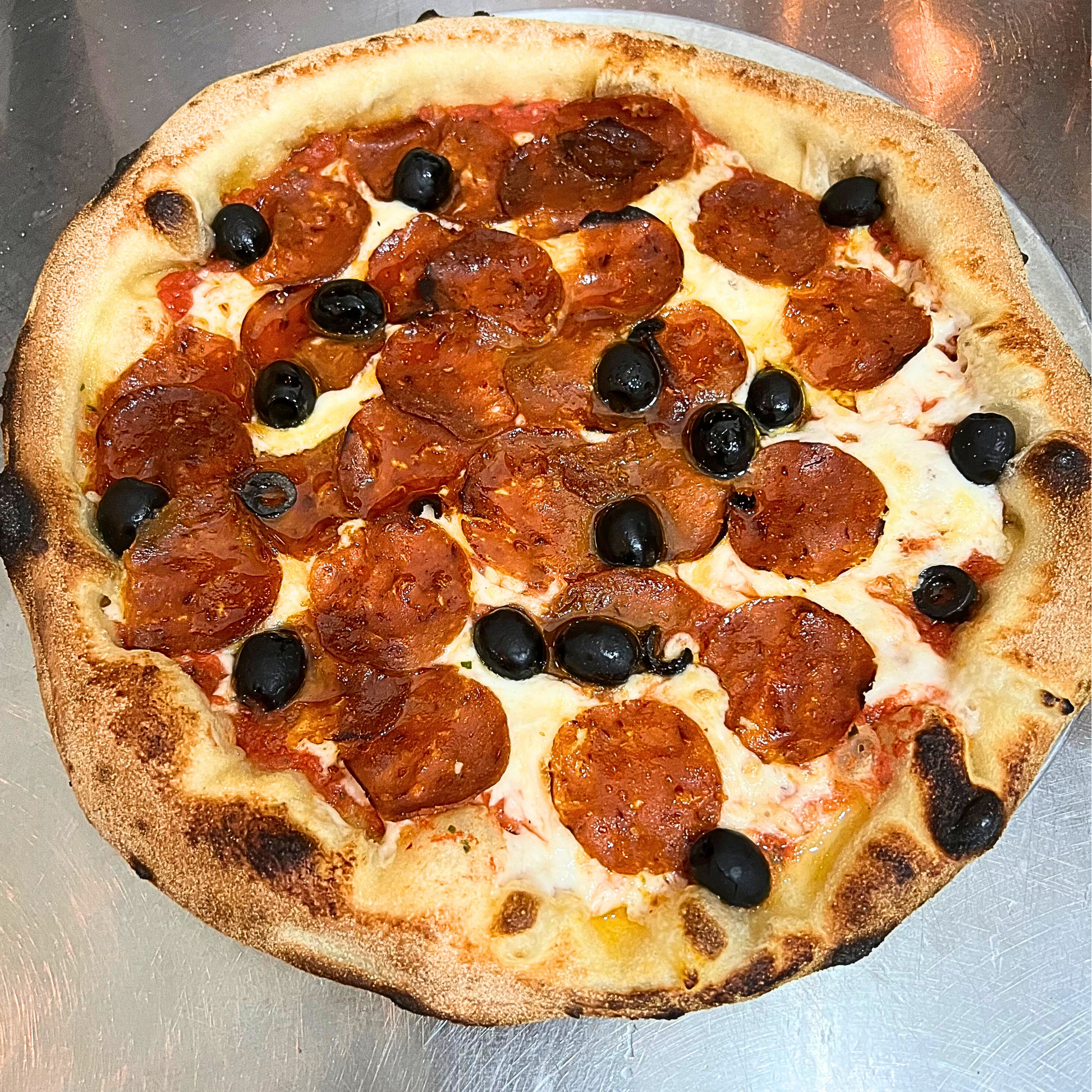 vegan pizza topped with vegan pepperoni, melted vegan mozzarella and black olives, serving suggestion