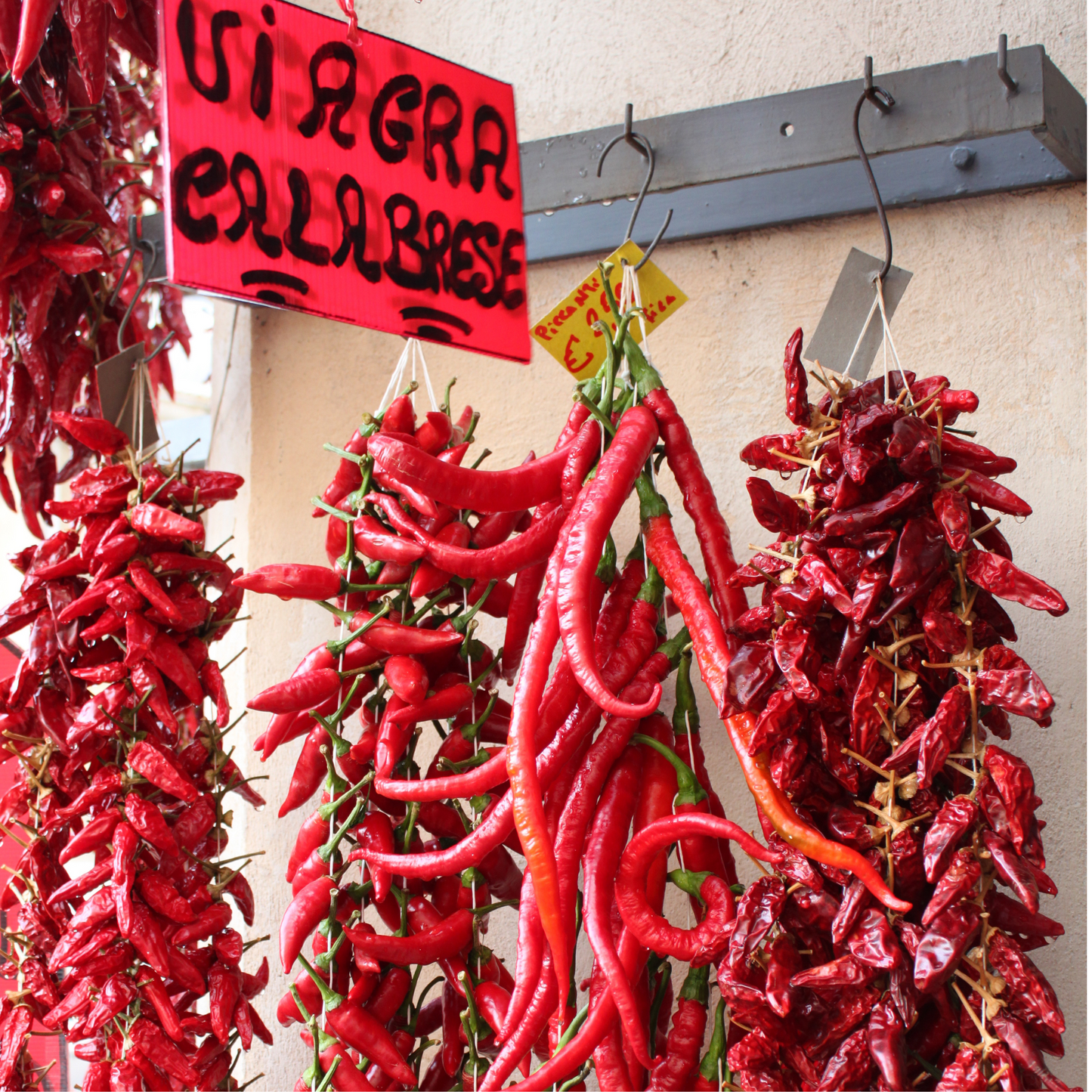 Chillies hanging from  hooks with a sign saying "viagra calabrese". Our vegan 'nduja uses chillies for their fiery taste