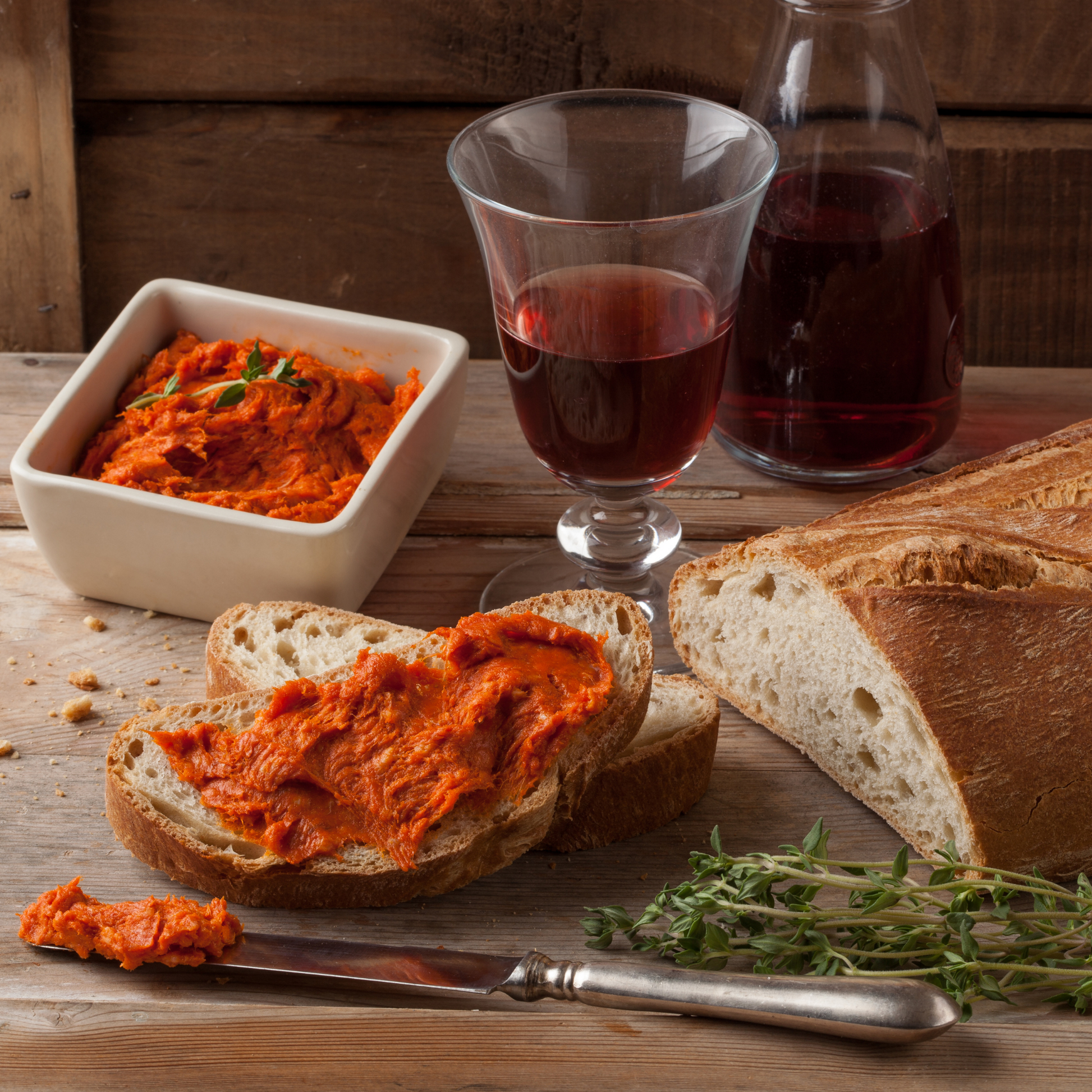 Vegan 'nduja being being spread with a butter knife on sourdough bread slice and being paired with a glass of red wine, serving suggestion.